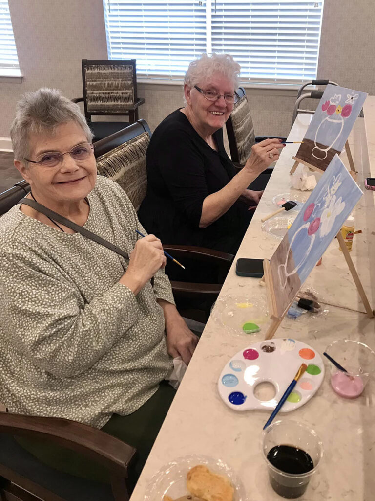 Two women, senior residents with paint brushes in hand, passionately create a masterpiece on canvas - a beautiful vase of flowers. Art knows no age limits!
