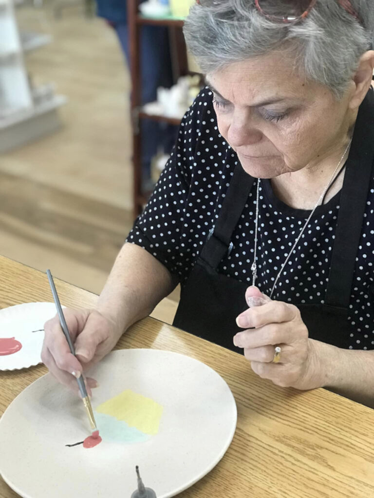 A senior woman painting a plate with a cupcake design, complete with a cherry on top.
