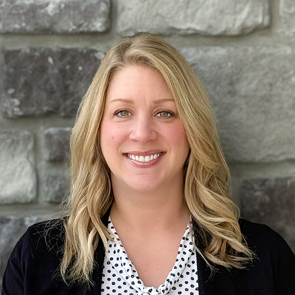 Amanda Bernhardt, Senior Living Director at The Boulevard Saint Peters Senior Living, smiling in front of a gray stone wall, wearing a polka-dot blouse and black cardigan.