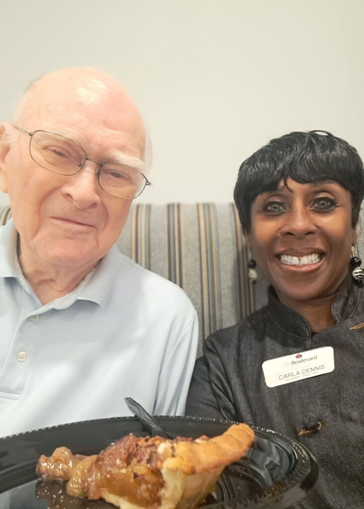 Culinary Director Carla Dennis smiles with a senior resident at The Boulevard, sharing a slice of pecan pie together during a community dining experience.