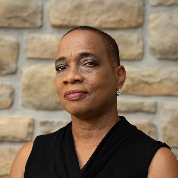 Carmen Smith, Memory Care Director at The Boulevard Saint Peters Senior Living, in a professional headshot. She has short hair, wears a black sleeveless blouse, diamond-shaped earrings, and dark glasses in some images, standing in front of a light stone wall background.