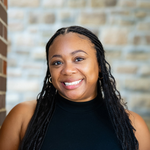 Ashley Moore, Executive Director Interim at The Boulevard Senior Living of Saint Peters, smiling warmly while wearing a sleeveless black top, standing in front of a light stone wall with a softly blurred background.