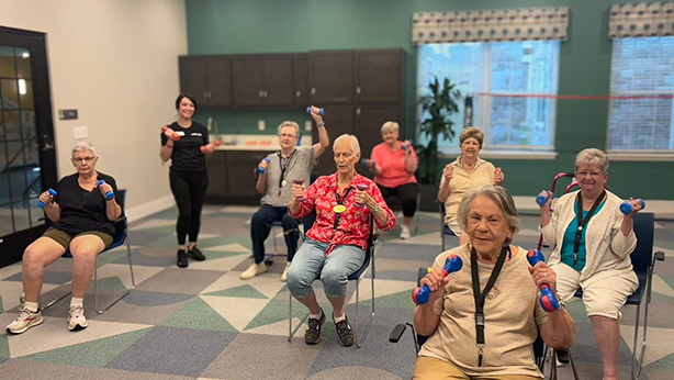 Seniors and team members lift hand weights while participating in an exercise session in the fitness center.