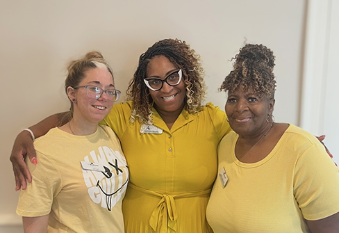 Three women on the Boulevard St. Peters team smile, wearing yellow, at a community event.