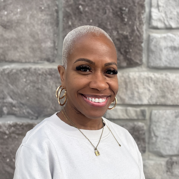 Lashantey Carter, Memory Care Director at The Boulevard Senior Living of Saint Peters, smiling in a professional headshot, wearing a white top and gold hoop earrings, with a stone wall background.
