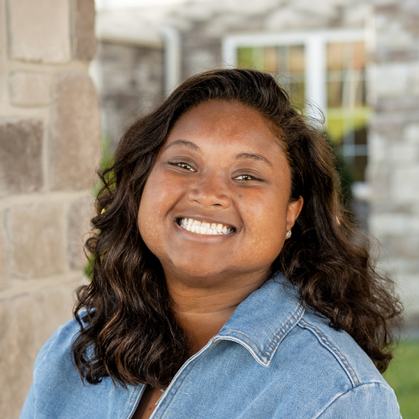 Catherine Alexander, Wellness Director at The Boulevard Senior Living of St. Peters, smiling in a professional outdoor headshot with shoulder-length wavy dark hair, a denim jacket, and a softly blurred stone building background.